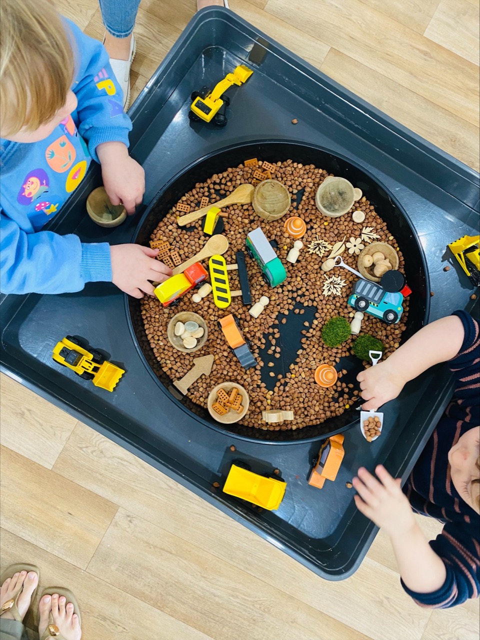 Children exploring a natural sensory tray with wooden vehicles at B.Curious